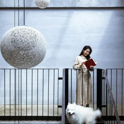 woman in beige shirt dress holding a book beside white furry dog